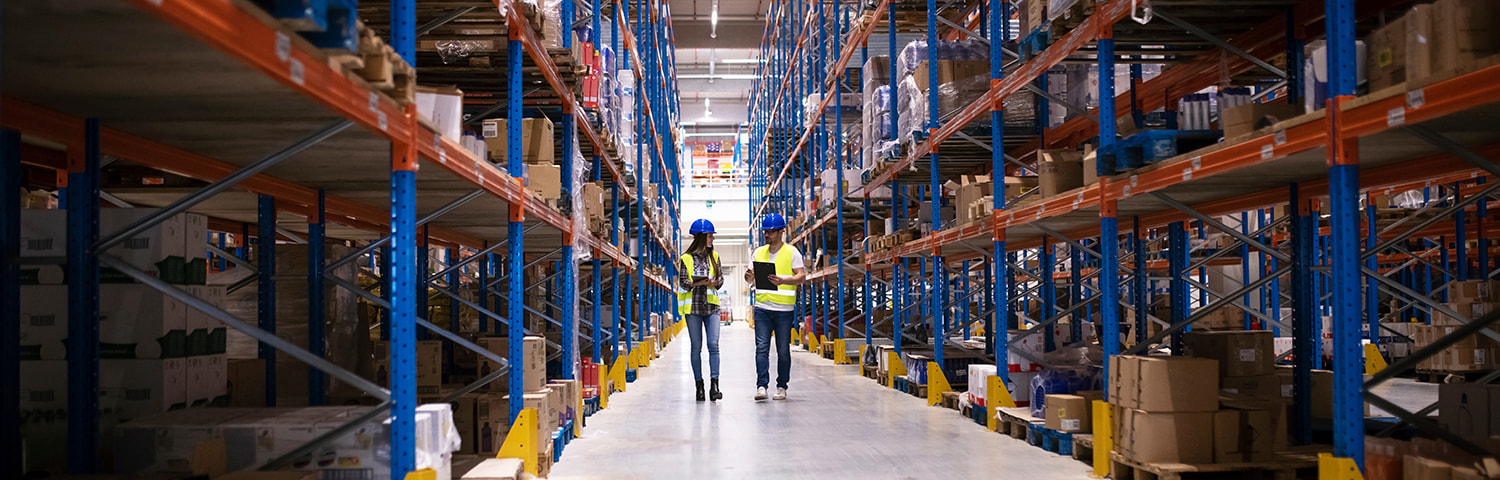 female and male walking in an aisle of pallet rack in a warehouse