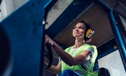 female wearing safety vest and safety earmuffs driving a forklift