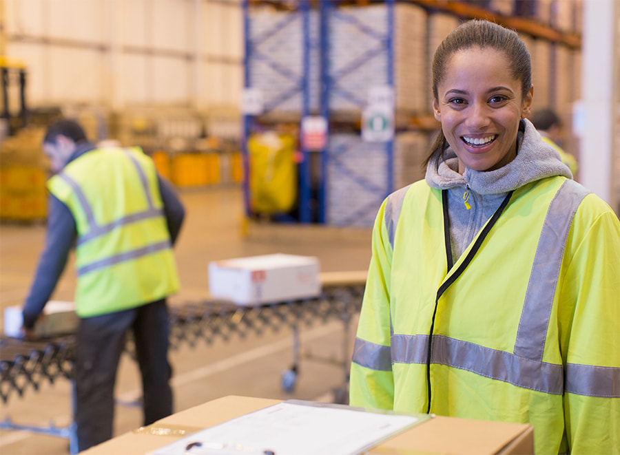female wearing safety vest working in a warehouse smiling