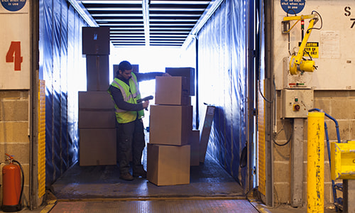 male scanning boxes in an open trailer parked in a loading dock
