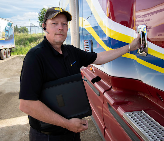 male wearing a Tag Logistics hat holding a clip board opening the door to a red semi-truck